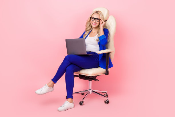 迷人的专业女士的全身照片坐办公椅使用技术笔记本电脑穿西装眼镜孤立的粉红色背景图片下载