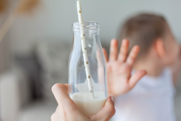 可爱快乐的金发男孩穿着轻薄的衣服拒绝在家里喝牛奶。生态产品。健康的食物和饮料。图片下载
