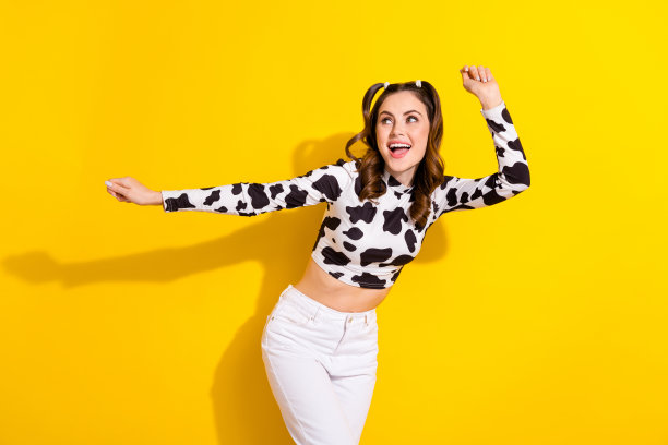 甜美可爱的女士穿着牛皮衬衫微笑跳舞，有乐趣孤立的黄色背景的照片图片下载