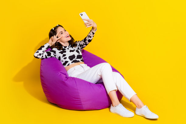 可爱时髦的女士穿着牛皮衬衫坐在豆袋录制视频博客空白空间孤立的黄色背景的照片图片下载