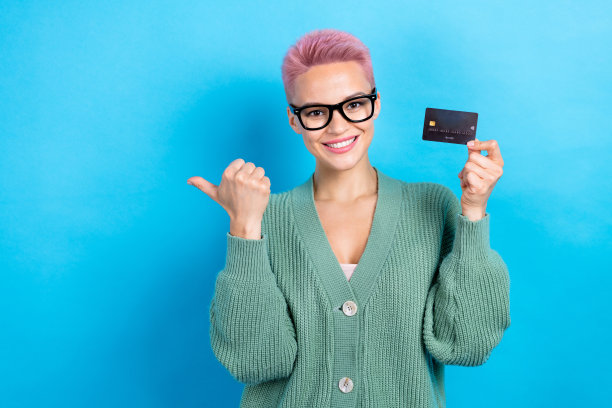 照片中可爱的美女穿着时尚的衣服，手臂拿着塑料卡片，在蓝色的背景上展示了空白的空间图片下载