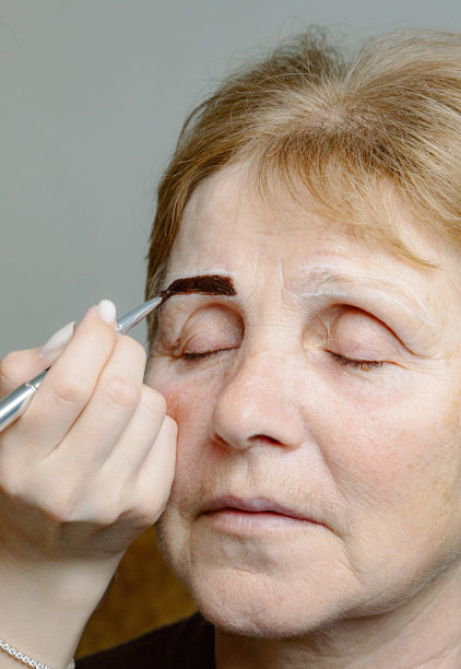 一位美容师在给一位老妇人画眉毛。图片下载