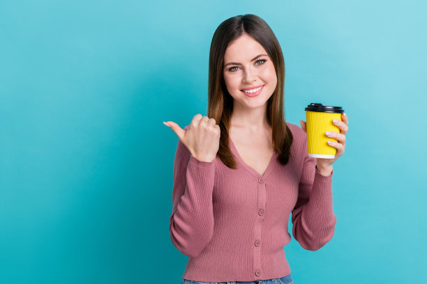 年轻迷人的女孩的照片拿着塑料杯咖啡指导手指空的空间最好的拿铁喝咖啡馆孤立的蓝色背景图片下载