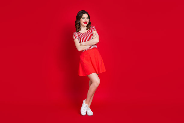 全身照片可爱的女孩看空空间广告宣传双臂交叉穿上衣裙子运动鞋孤立的红色背景图片下载