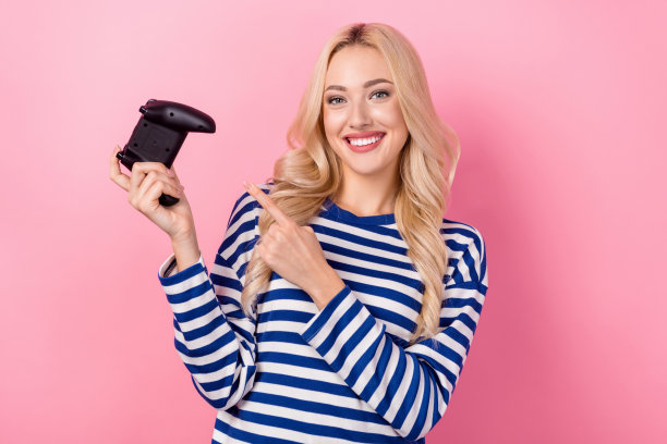 照片中，乐观的年轻女孩穿着条纹套头衫，用手指着她的xbox游戏机手柄上瘾的玩家，背景是粉红色的图片下载