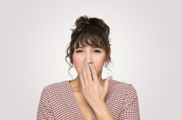 疲惫不堪:穿着休闲条纹衬衫的疲惫年轻女子捂住嘴忍住打哈欠图片下载