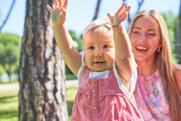 在阳光明媚的公园里，宝宝高高举起双手，在妈妈的陪伴下享受着快乐的时刻图片下载