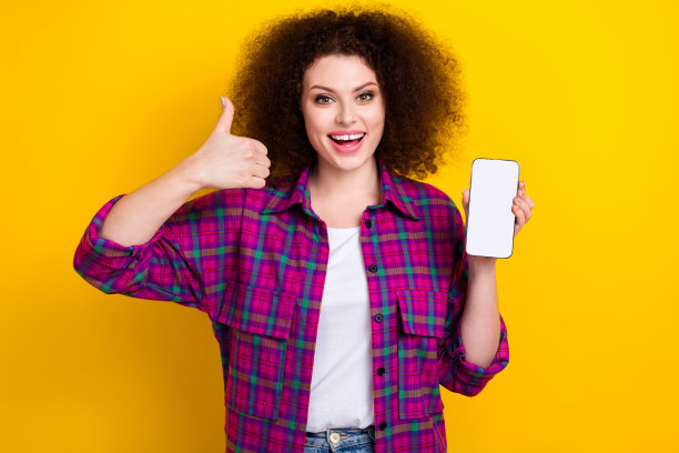 年轻女士穿着格子衬衫的照片大拇指向上推荐新的应用程序网站送餐手拿手机屏幕孤立的黄色背景图片下载
