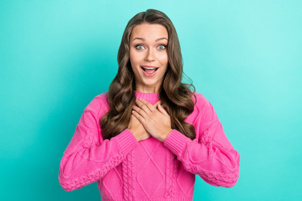 照片的开朗惊讶的女人波浪发型穿着针织衫毛衣手臂在胸前印象深刻凝视孤立在蓝绿色的背景图片下载
