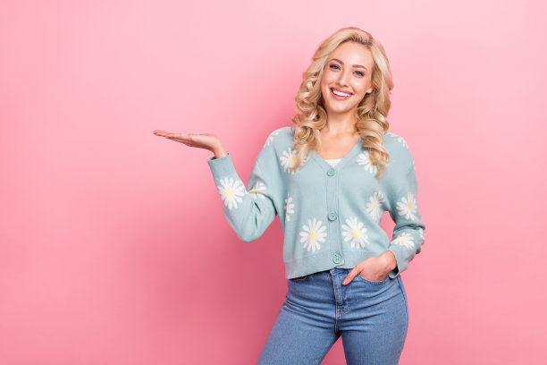 年轻漂亮的女人穿着衬衫的照片，雏菊印花的魅力装，挽着手臂展示新产品孤立在粉红色的背景图片下载