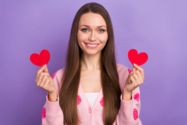 年轻漂亮的女人的照片穿着粉红色的开襟羊毛衫草莓装饰拿纸爱心蜜月孤立在紫色的背景图片下载