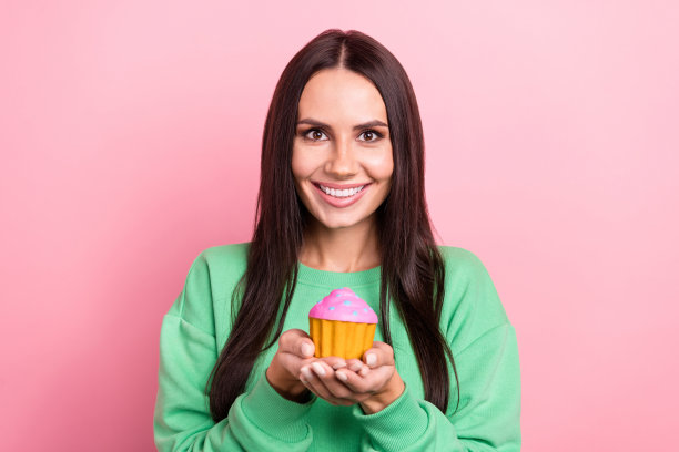 好心情的肖像好可爱的女孩直发穿绿色套头衫拿着美味的蛋糕孤立在粉红色的背景图片下载