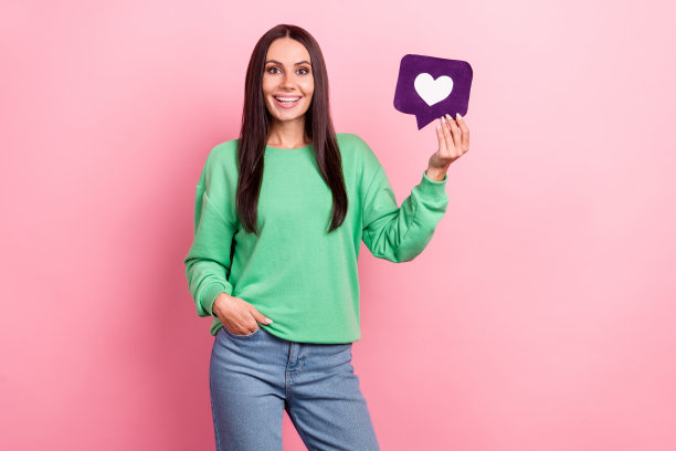 开朗可爱的女孩穿着绿色套头衫的肖像，影响者博主拿着像粉色背景上孤立的图标图片下载