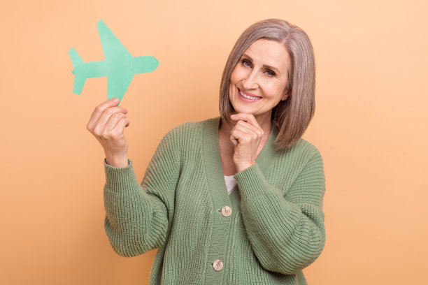 满意的退休女士的照片，穿着卡其色衬衫，拿着纸折纸飞机旅游检票，在米色背景上孤立图片下载
