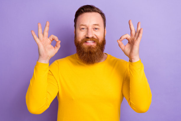 照片中年轻的商人穿着黄色的套头衫，显示出满意的双ok标志，高质量的产品被隔离在紫罗兰色的背景上图片下载