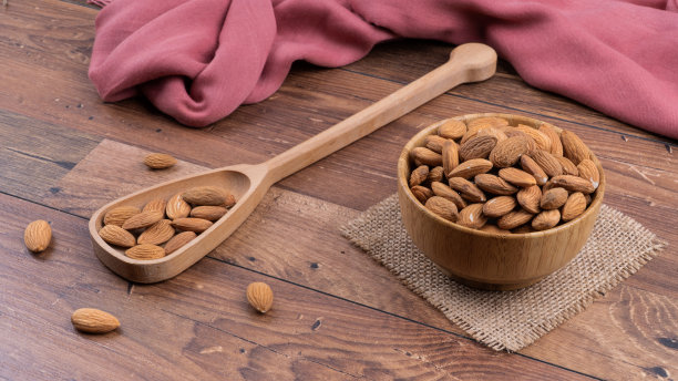 照片上的新鲜杏仁质朴的木制背景。木碗装杏仁。在碗旁边，木勺里的更多杏仁被放在一个木制的表面上。图片下载
