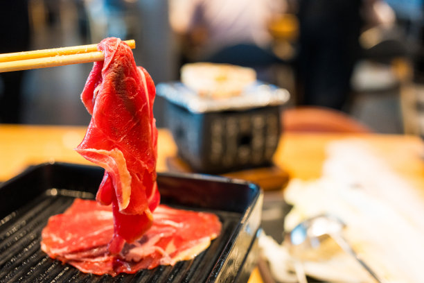 特写镜头:筷子从托盘里夹起多汁的牛肉片，放入火锅中煮。图片下载