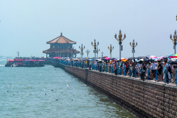 湛桥码头和惠兰亭伸入大海，在炎热的夏天，许多游客带着雨伞游览青岛码头图片下载