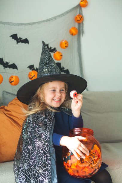 可爱的小女孩3岁，穿着女巫服装，拿着装满糖果的南瓜桶在家里庆祝万圣节。图片下载