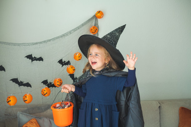 可爱的小女孩3岁，穿着女巫服装，拿着装满糖果的南瓜桶在家里庆祝万圣节。图片下载