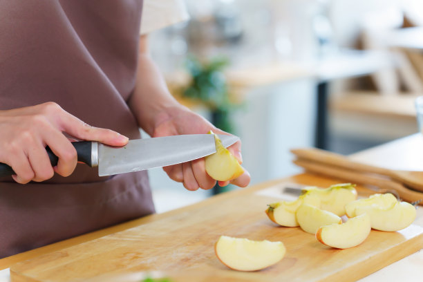 亚洲妇女用刀在砧板上切苹果片的特写手，准备水果和新鲜蔬菜的原料，烹饪早餐，同时营造健康的饮食生活方式图片下载