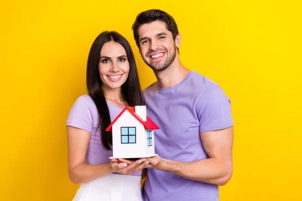 照片肖像迷人的年轻女子男子抱着小房子房地产穿时髦的紫色服装孤立在黄色的背景图片下载