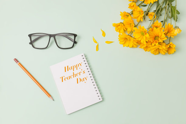 一束黄色的雏菊花，时髦的黑色眼镜，一支木制铅笔，笔记本上写着淡绿色背景的“教师节快乐”图片下载