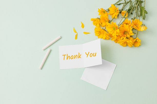 一束黄色的雏菊花，白色的粉笔，淡绿色背景上写着“谢谢”的贺卡，这是教师节的俯视图图片下载