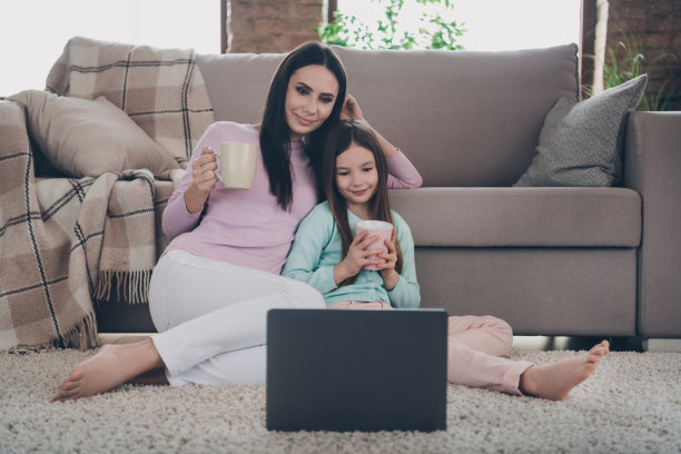 妈妈和小女儿周末的照片看上网本笔记本电脑电影坐在舒适的沙发地毯家公寓房子图片下载