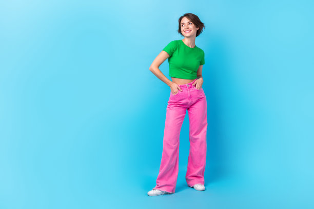 梦幻女士的全身照片穿绿色t恤粉红色裤子双手口袋空的空间廉价服装和孤立的海蓝宝石色背景图片下载
