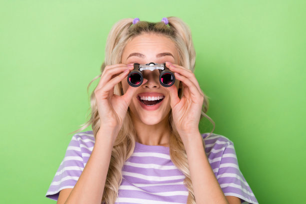 照片时髦的印象女士穿着紫色t恤做调查放大双筒望远镜孤立的绿色背景图片下载