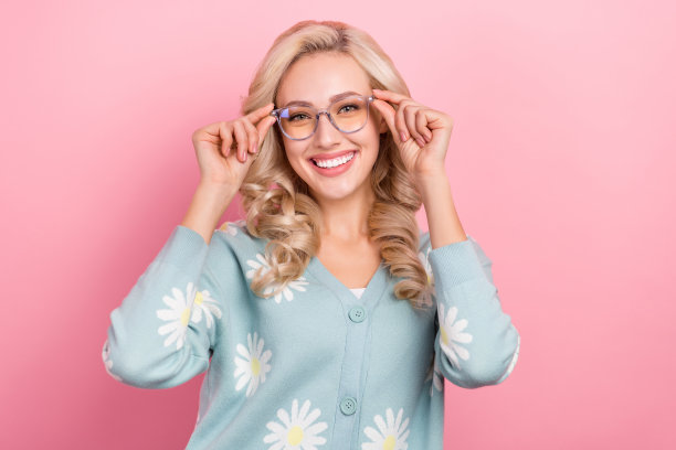 肖像照片的年轻华丽的微笑金发卷发女人触摸眼镜广告视觉眼镜店孤立的粉红色背景图片下载