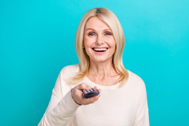 特写照片兴奋有趣乐观的高级妇女穿着时尚的白衬衫拿着遥控器电源按钮电视孤立在蓝色的背景图片下载