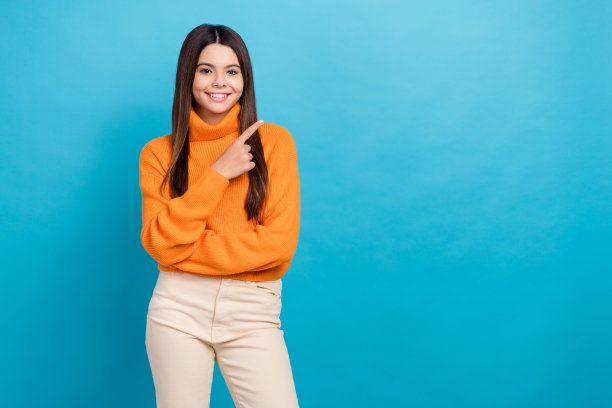 乐观满意的女孩的照片，长发，穿着针织高领衫，在蓝色背景上提供孤立的空间图片下载