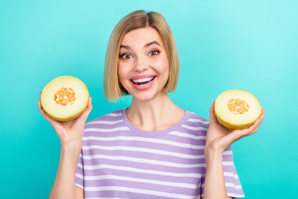 照片中的年轻兴奋积极的女孩拿着两片新鲜水果成熟的夏瓜吃维生素促进青色背景隔离图片下载