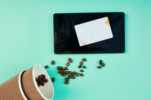 洒在外卖杯和平板电脑附近的咖啡豆，背景是蓝绿色的信用卡图片下载