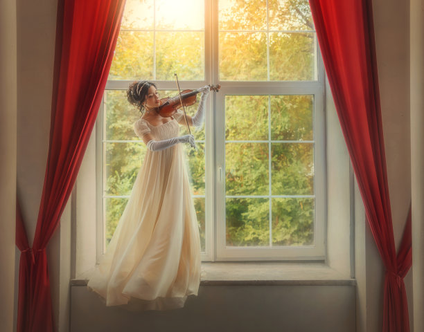 艺术照片真人。幻想女人小提琴手拉小提琴经典的老式女孩站在窗台上绿色花园阳光。美女的脸庞白色的复古长裙随风飘动图片下载