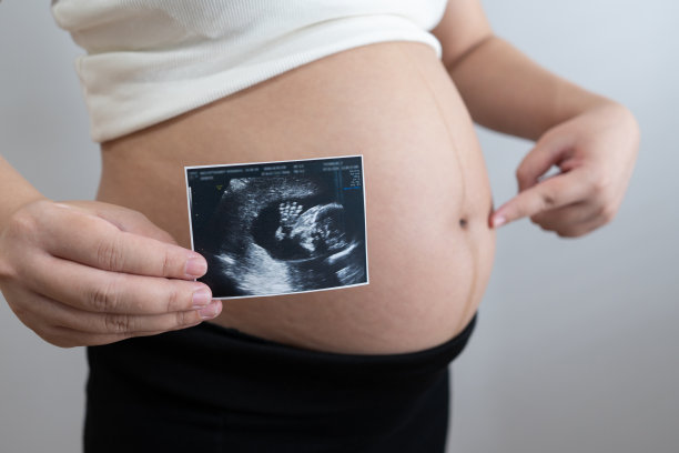 一名孕妇拿着婴儿的超声波照片，微笑着凝视着这张照片。超声波显示了胎儿发育的清晰画面，捕捉到了母亲和期待的珍贵时刻。图片下载