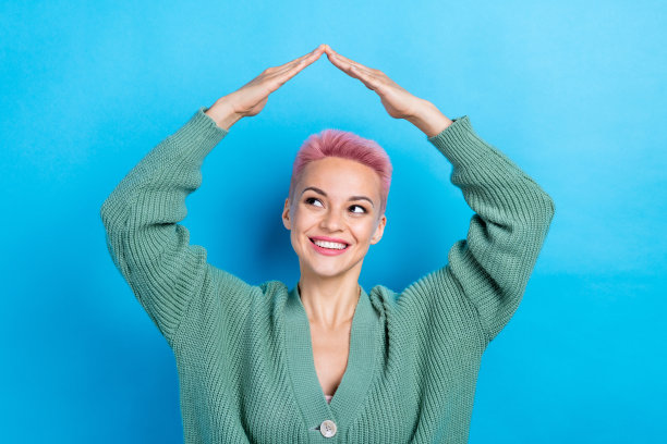 照片中积极的女士穿着时髦舒适的衣服，两只手臂在头下，在蓝色的背景下，房子的屋顶看起来很空旷图片下载