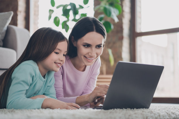 照片中可爱闪亮的妈妈女儿穿着休闲装准备家庭作业在室内的现代设备图片下载