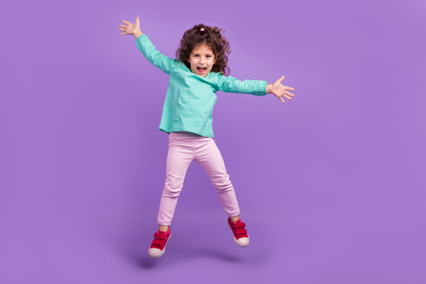 时髦兴奋的小孩穿着蓝绿色的衬衫跳高像星星孤立的紫色背景的全长照片图片下载
