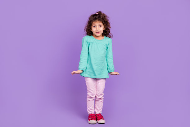 甜美困惑的小孩穿绿松石衬衫的全身照片耸肩孤立的紫罗兰色背景图片下载