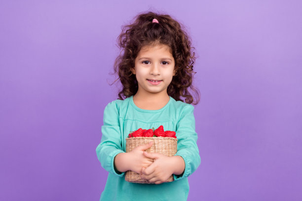 照片中可爱可爱的小孩穿着蓝绿色的衬衫，收集满草莓篮子，孤立的紫罗兰色背景图片下载