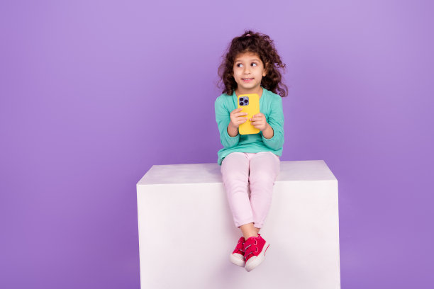 照片中可爱体贴的小女孩穿着蓝绿色的衬衫，发短信给现代的小工具，看起来空无一物，孤立的紫色背景图片下载