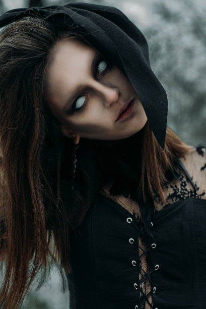 一个年轻女子在哥特式阴森的形象，一个女巫在阴森的森林万圣节服装。垂直的照片。图片下载