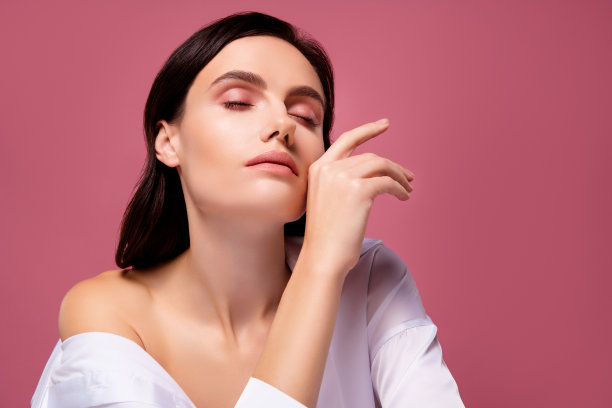 照片的黑发女孩触摸手指，脸感到温柔，闭上眼睛孤立的粉红色背景图片下载