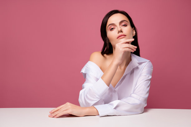 照片黑发女孩触摸下巴坐桌子感觉激情孤立柔和的粉红色背景图片下载