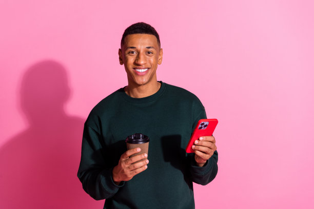 照片帅哥好心情穿运动衫喝饮料阅读现代小工具空旷的空间孤立的粉红色背景图片下载