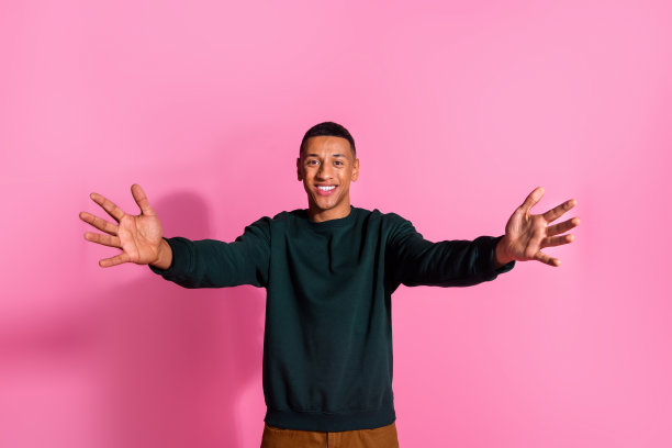 照片中有魅力的搞笑小伙穿着运动衫张开双臂准备拥抱你空旷的空间孤立的粉红色背景图片下载