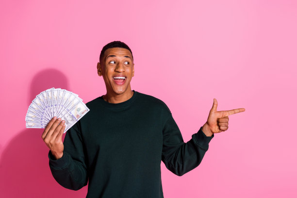 照片中的帅哥好心情穿着运动衫上升现金风扇显示空间空旷孤立的粉红色背景图片下载